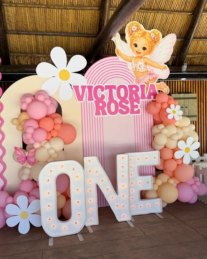 Light-up ONE letters at a first birthday with daisy cutouts and a coral garland