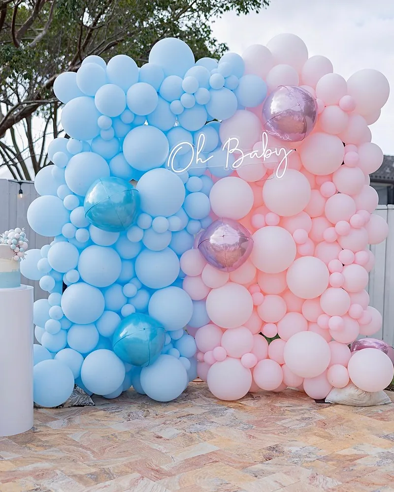 A gender reveal balloon wall, half blue and half pink, with an Oh Baby neon sign