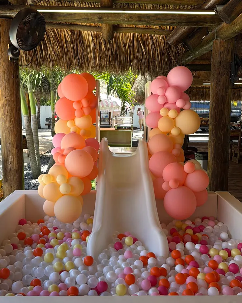 A ball pit with a slide framed by balloon columns